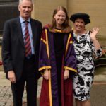 Me and my parents smiling and laughing at my PhD graduation. I'm wearing a long red and purple robe trimmed with bright yellow. My mum is wearing the black wide rimmed hat with a yellow tassle and waving at the camera.
