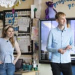 Lizzie standing in a primary school classroom with primary school teacher Joshua Piggott.