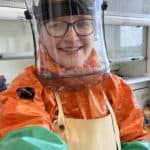 Female dressed in PPE in a lab.