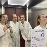 Group of 4 ladies in lab coats smiling in a mirror selfie