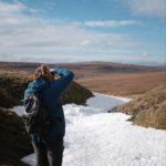 Woman in blue coat taking a photo of a patch of snow on a hill in Northern England.
