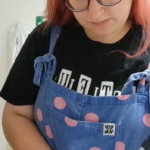 A red-haired person wearing blue spotty dungarees and purple gloves pipetting.