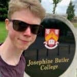 A picture of Ollie in front of a plaque with the coat of arms of Josephine Butler College on it.