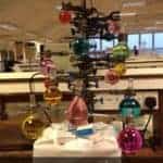 A clamp stand with various flasks of coloured liquid arranged to look like baubles on a Christmas tree