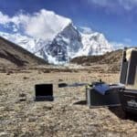 A drone and a computer resting on the ground in front of a mountain.