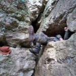 A pair of legs emerging from a narrow cave part way up a cliff.