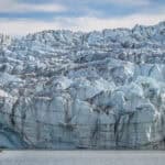 A small red kayak in front of a towering wall of blue ice.