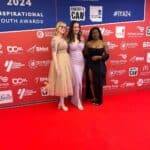 Three women posing in front of a red and blue background and red carpet