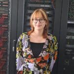 Ginger woman standing in front of server racks