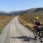 Person on a bike with on a gravel road going into the distance with green hills in the background