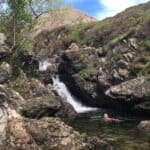 Person swimming in a pool at the bottom of a waterfall