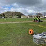 A photo of a park with a metal box, laptop, cables and students in hi-viz vests - surveying for geothermal resources.