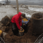 A photo of me digging up an instrument surrounded by mud and an upturned plastic bin, in the snow.