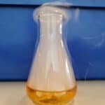 A conical flask with yellow/orange liquid at the bottom with vapour above from adding dry ice to the liquid