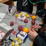 A science room desk with multiple voltmeters connected to fruits and vegetables via wires