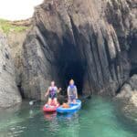 Two people on paddleboards in front of a cave