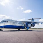 Blue and white research aircraft parked outside on apron. Green grass and blue sky with clouds in background.