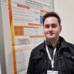 A picture of me at a conference in Italy presenting a poster of my work