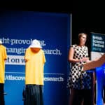 Laura on a stage with 2 manekins wearing yellow tshirst/
