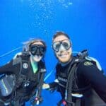 Two people in dive gear underwater, with blue sea behind them