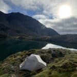 Tent on grass foreground with lake and hill behind