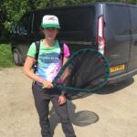 A woman with an insect net wearing a hat and a bright coloured tshirt.